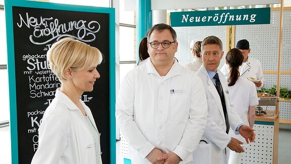 Dr. Kaminski, Pfleger Hans-Peter Brenner und Dr. Kathrin Globisch stehen in der Cafeteria in einer Schlange.