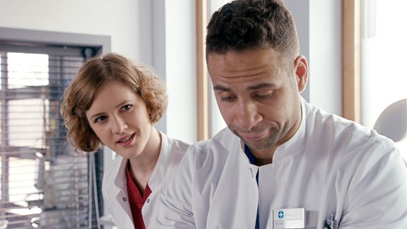 Eine Ärztin blickt fragend zu einem Gesprächspartner. Schräg vor ihr steht ein weiterer Arzt.