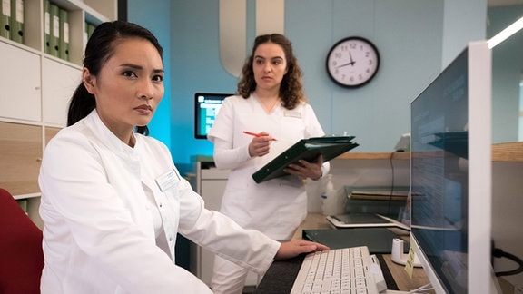 Dr. Lilly Phan (Mai Duong Kieu, li.) liest bei Dienstbeginn einen bekannten Namen unter den Patientendaten. Schwester Jasmin Hatem (Leslie-Vanessa Lill, re.) kann der Ärztin sagen, wo sie ihn findet.