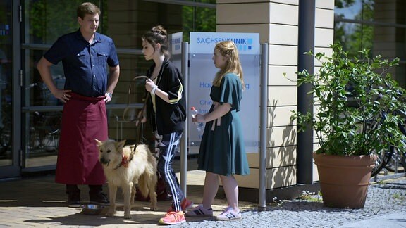 Ein Mann und zwei Frauen mit einem Hund vor der Sachsenklinik