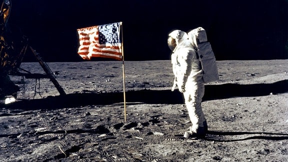 Astronaut Edwin 'Buzz' Aldrin steht neben einer US-Flagge auf der Mondoberfläche.