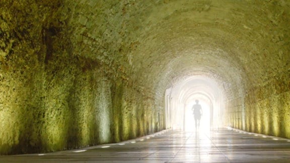 Eine Person steht in einem Tunnel, an dessem Ende ein grelles strahlendes Licht einfällt.