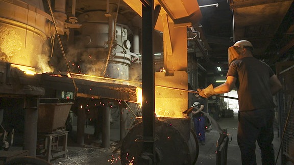 Ein Arbeiter mit Schweißermaske arbeiten an einem Ofen in einer Fabrik.
