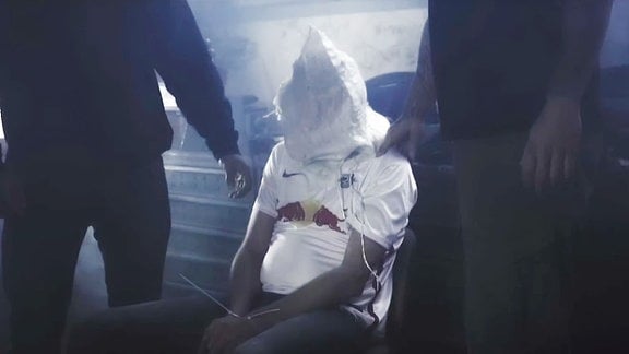 In einem Musikvideo wird ein Mann mit einem RB Trikot in einem Keller gefesselt