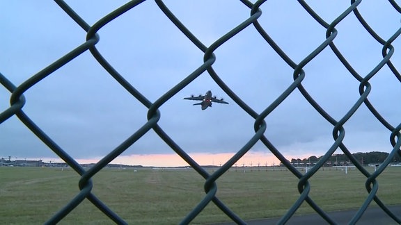 Ein Zaun an einem Flugplatz. Ein Flugzeug hebt ab.