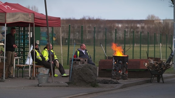 Drei Streikende sitzen um eine brennende Tonne.