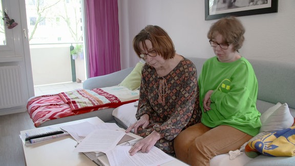Zwei Frauen sitzen auf einem Sofa und schauen sich Dokumente an.