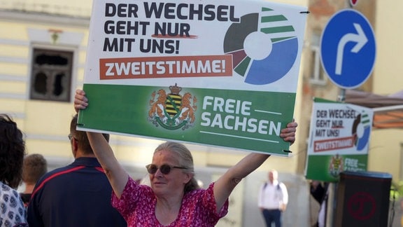 Eine Frau hält ein Wahlplakat der Freien Sachsen hoch.