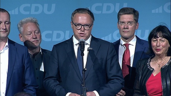 Politiker*innen der CDU stehen gemeinsam an einem Mikrofon auf einer Bühne.