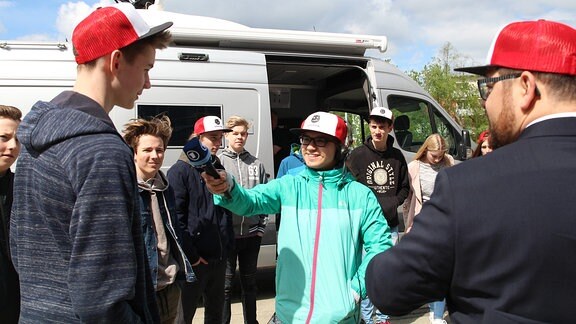 Ein Junge hält in Mitten einer Gruppe junger Menschen ein Mikrofon.