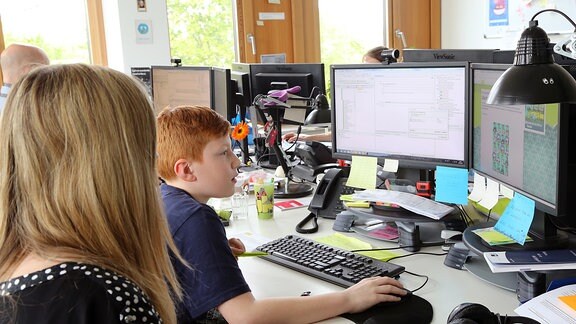 Ein Junge und ein Mädchen sitzen vor zwei Computerbildschirmen.