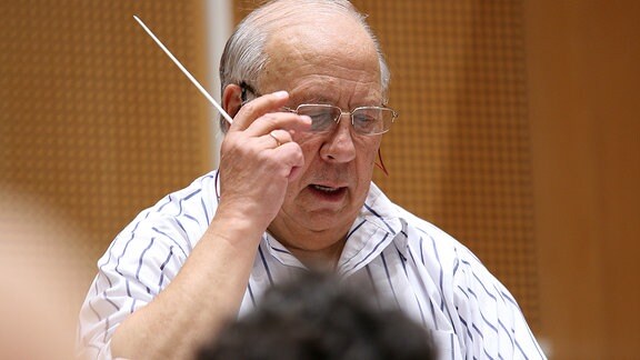 Dirigent Neeme Järvi mit Taktstock - fasst sich an seine Brille.