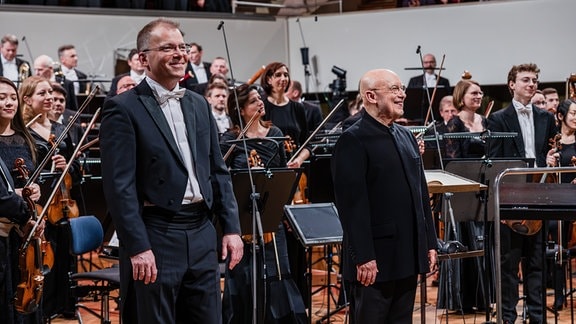 Philipp Ahmann und Dennis Russell Davies beim Schlussapplaus auf der Bühne des Leipziger Gewandhauses beim Festkonzert zum 100. Geburtstag der MDR-Ensembles