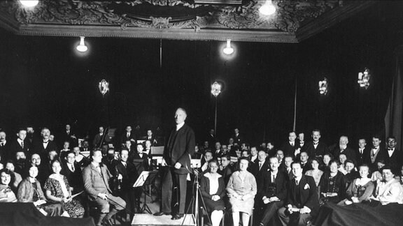 Historisches Schwarz-weiß-Bild zeigt das Leipziger Sinfonieorchester (LSO) mit der Oratorienvereinigung und Dirigent Alfred Szendrei in den 1920er Jahren in der Alten Handelsbörse in Leipzig.