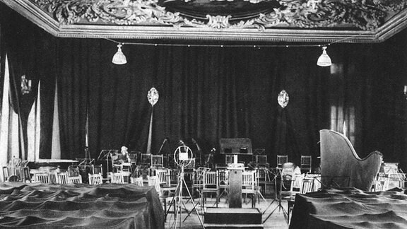 Historisches Schwarz-weiß-Bild: In der Alten Handelsbörse in Leipzig ist ein Senderaum aufgebaut, Instrumente stehen zwischen Mikrofonen und Stühle im Bühnenbereich.