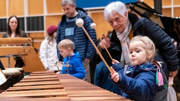 Ein Kind schlägt mit einem Schlägel auf ein Marimbaphon. 