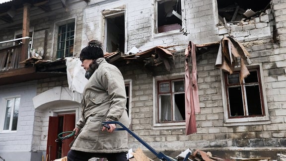 Krieg in der Ukraine: Eine Frau zieht einen Handwagen durch eine von Bomben beschädigte Straße.