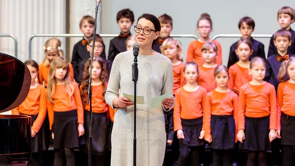 Nathalie Wappler Hagen steht vor einem Mikrofon, im Hintergrund der MDR-Kinderchor