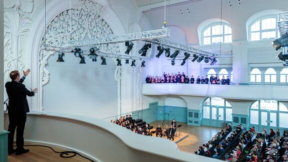 In der Leipziger Kongresshalle dirigiert Alexander Schmitt von einer Empore aus den MDR-Kinderchor auf der gegenüberliegenden Empore.