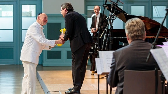 Ein Mann im weißen Anzug überreicht Blumen an Gunter Berger, den ehemaligen Leiter des MDR-Kinderchors.