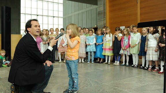 Der MDR-Kinderchor mit seinem damaligen Leiter Gunter Berger bei einem Konzert zum Kindertag 2011 im Museum der bildenden Künste in Leipzig. Gunter Berger kniet mit einem Mikrofon vor einem kleinen Mädchen.