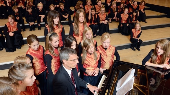 Kinder des MDR-Kinderchors stehen in Chorkleidung um einen Konzertflügel, an dem ihr damaliger Chorleiter Ulrich Kaiser spielt.