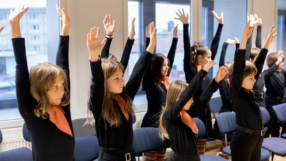 Die jungen Sängerinnen und Sänger des MDR-Kinderchors strecken beim Einsingen ihre Arme nach oben.