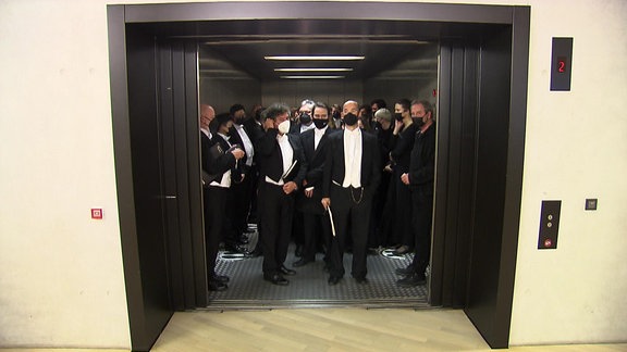 Mehrere menschen mit förmlicher Kleidung in einem Aufzug. 