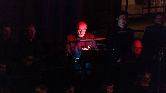 Der Tenor Kristian Sørensen in rotem Licht bei der Uraufführung von James MacMillans Werk "Ordo Virtutum" beim Nachtgesang am 26. Januar 2024 in der Leipziger Peterskirche.