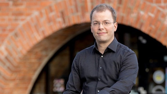 Philipp Ahmann, Künstlerischer Leiter des MDR-Rundfunkchors, sitzt auf einer Mauer
