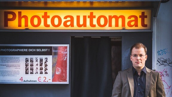 Philipp Ahmann, Künstlerischer Leiter des MDR-Rundfunkchors, lehnt an einem Fotoautomaten