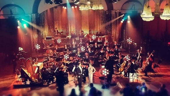 Im Scheinwerferlicht musiziert im Leipziger Felsenkeller das MDR-Sinfonieorchester, davor die drei schick gekleideten Gesangssolisten und das Publikum an Tischen sitzend.
