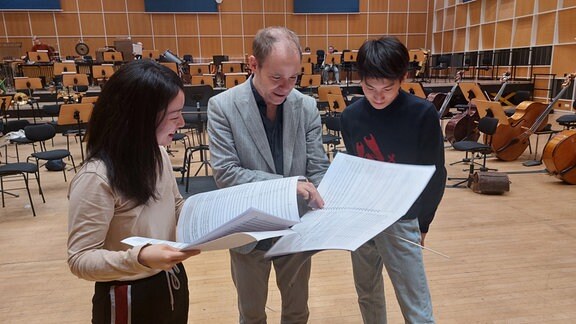 Dirigent Michael Wendeberg gibt Kompositionsstudentin Haonan Guo und Kompositionsstudenten Zhaolong Sun Verbesserungsvorschläge
