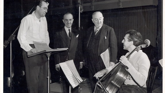 Drei Männer, darunter Komponist Thomas de Hartmann, reden auf dieser alten Schwarz-Weiß-Aufnahme mit dem sitzenden Cellisten Paul Tortelier.