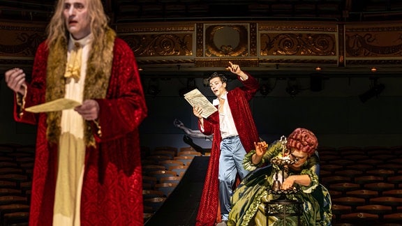 Szene aus dem Stück "Amadeus" über Mozart, zu sehen sind zwei Männer und eine Frau in den typischen Kostümen der Rokoko-Zeit