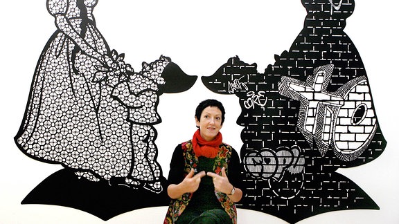 Die Künstlerin Annette Schröter sitzt in ihrem Atelier in Leipzig vor ihrer über zwei Meter hohen und über drei Meter breiten Scherenschnittgruppe "Kindheitsmuster".