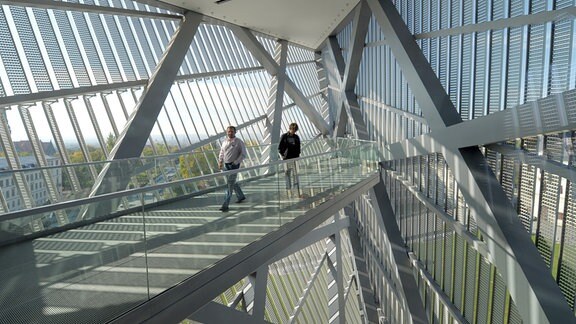 Besucher gehen im Militärhistorischen Museum der Bundeswehr in Dresden über eine Brücke zur glasverkleideten Spitze eines architektonischen Aluminiumkeils.
