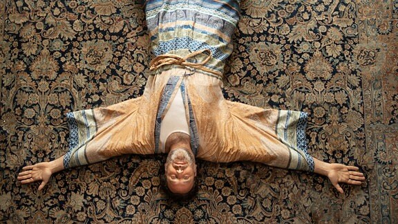 Musiker Chilly Gonzales liegt im seidenen Morgenmantel aud einem orientalischen Teppich.
