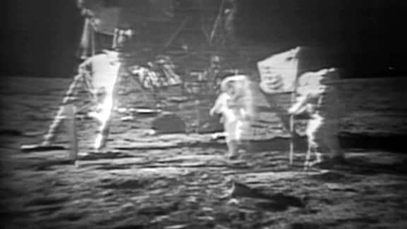 Astronauten stellen eine Flagge auf dem Mond auf.