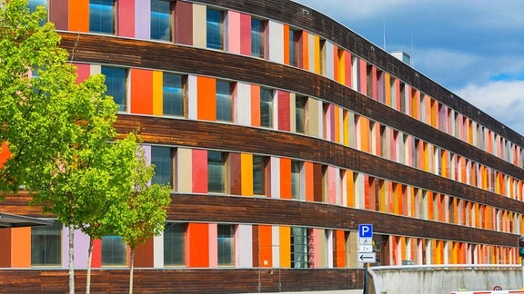 Blick auf das Umweltbundesamt in Dessau: Eine geschwungende Fassade mit bunten Holzplatten und zahlreichen Fenstervertiefungen.