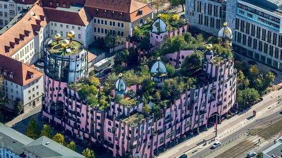 Luftaufnahme der Grünen Zitadelle in Magdeburg: Ein überwiegend rosafarbenes Gebäude mit Pflanzen auf den Dächern.
