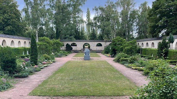 Das Kolumbarium auf dem Gertraudenfriedhof, umrandet von einer durch Bögen durchbrochenen Ziegelsteinmauer und in der Mitte der Grünfläche durch eine Skulpturengruppe verziert