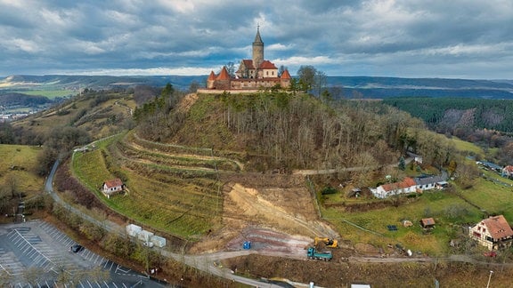 Zu sehen ist eine Drohnenaufnahme, die Burg Leuchtenburg steht auf einem Hügel, an dem Hügel finden Bauarbeiten statt.