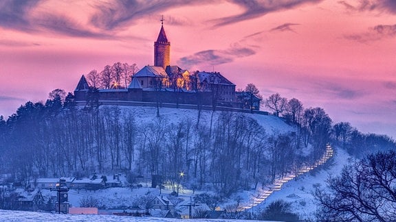 Eine Burg umgeben von Schnee und einem rosa Himmel.