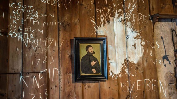 die Lutherstube, hier hatte der Reformator ab Dezember 1521 in gut zehn Wochen das Neue Testament aus dem Griechischen ins Deutsche uebersetzt, ehe er im Maerz wieder nach Wittenberg abreiste. Extra fuer die Nationale Ausstellung erlebt in dem historischen Raum ein Mythos Auferstehung: An der Wand erscheint von Zeit zu Zeit mittels Beamer der ominoese Fleck, der von einem Wurf Luthers mit seinem Tintenfass auf den Teufel herruehren soll.)