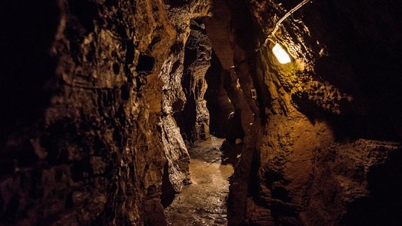 Blick in die Götz-Höhle: ein schmaler Gang zwischen Gesteinwänden, spärlich mit einer Lampe beleuchtet
