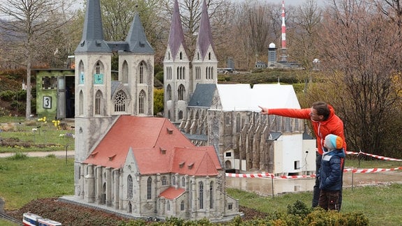 Ein Besucher weist seinen Sohn auf ein Modell der Martinikirche im Miniaturenpark Harz hin, im Hintergrund rechts eine Nachbildung des Halberstädter Doms. 