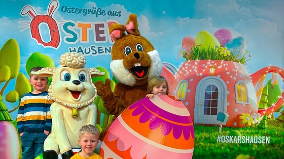 Drei Kinder posieren gemeinsam mit einem Osterhasen, großen Ostereiern und einer Schaf-Plastik an einem Fotospot in Oskarshausen.