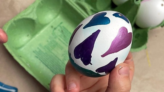 Zu sehen ist eine Kinderhand mit einem mit Herzen bemalten Ei.