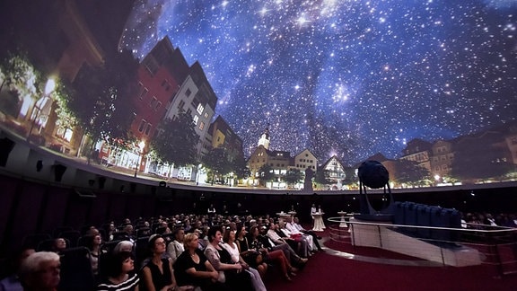 Planetarium Jena: Menschen sitzen auf Stühlen und blicken gebannt an die Projektionen eines Nachthimmels